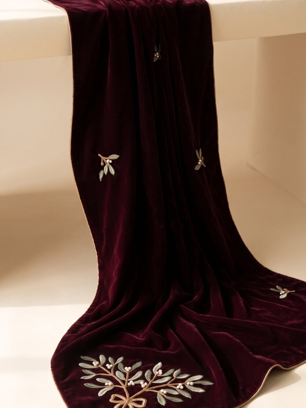 Deep burgundy velvet draping off a table with mistletoe embroidery